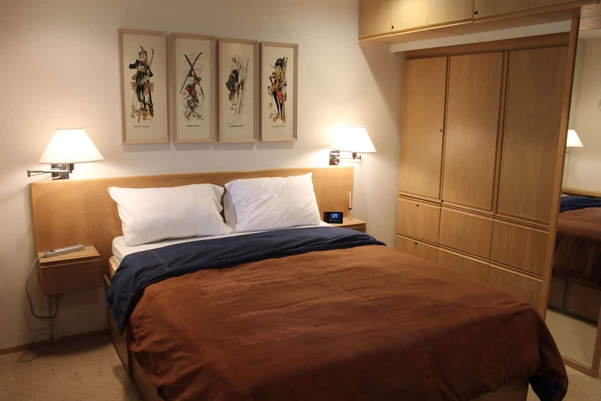 A neatly made bed with white and brown bedding, two bedside lamps, and a nightstand with a remote control.