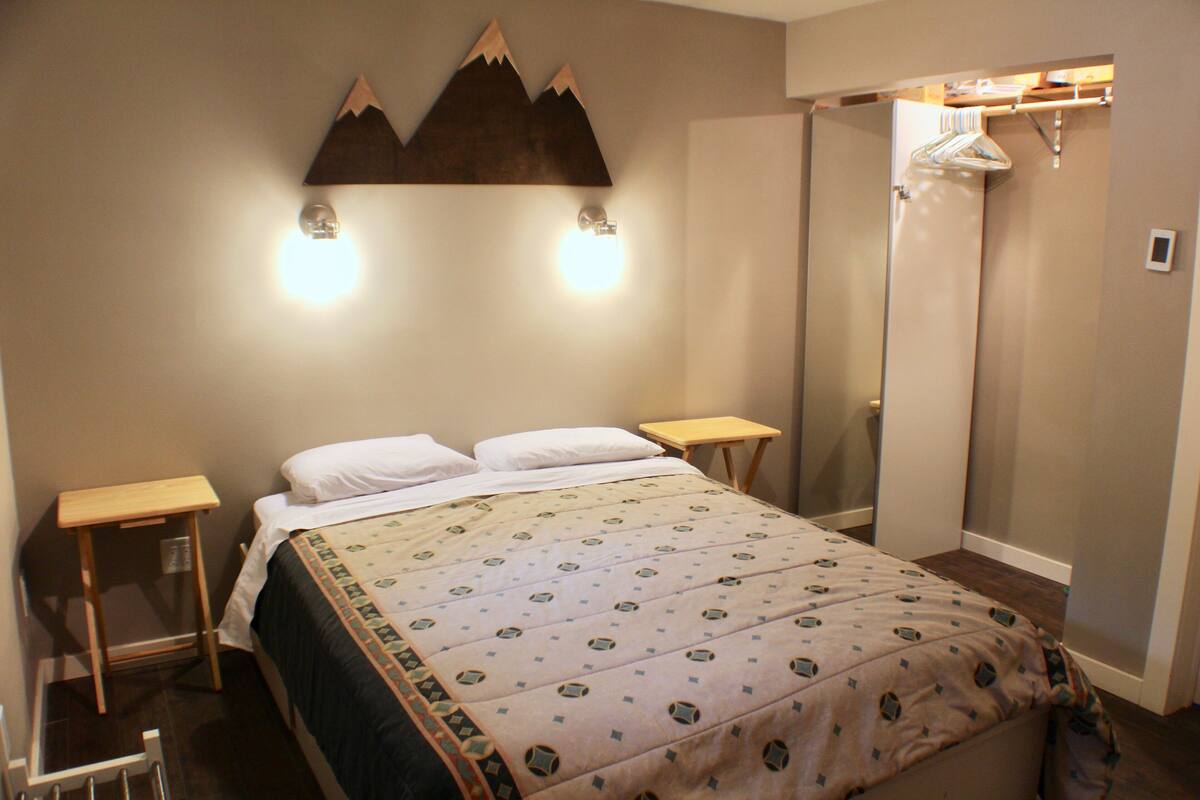 A neatly made bed with a patterned bedspread, two bedside tables, and a wall-mounted light fixture.