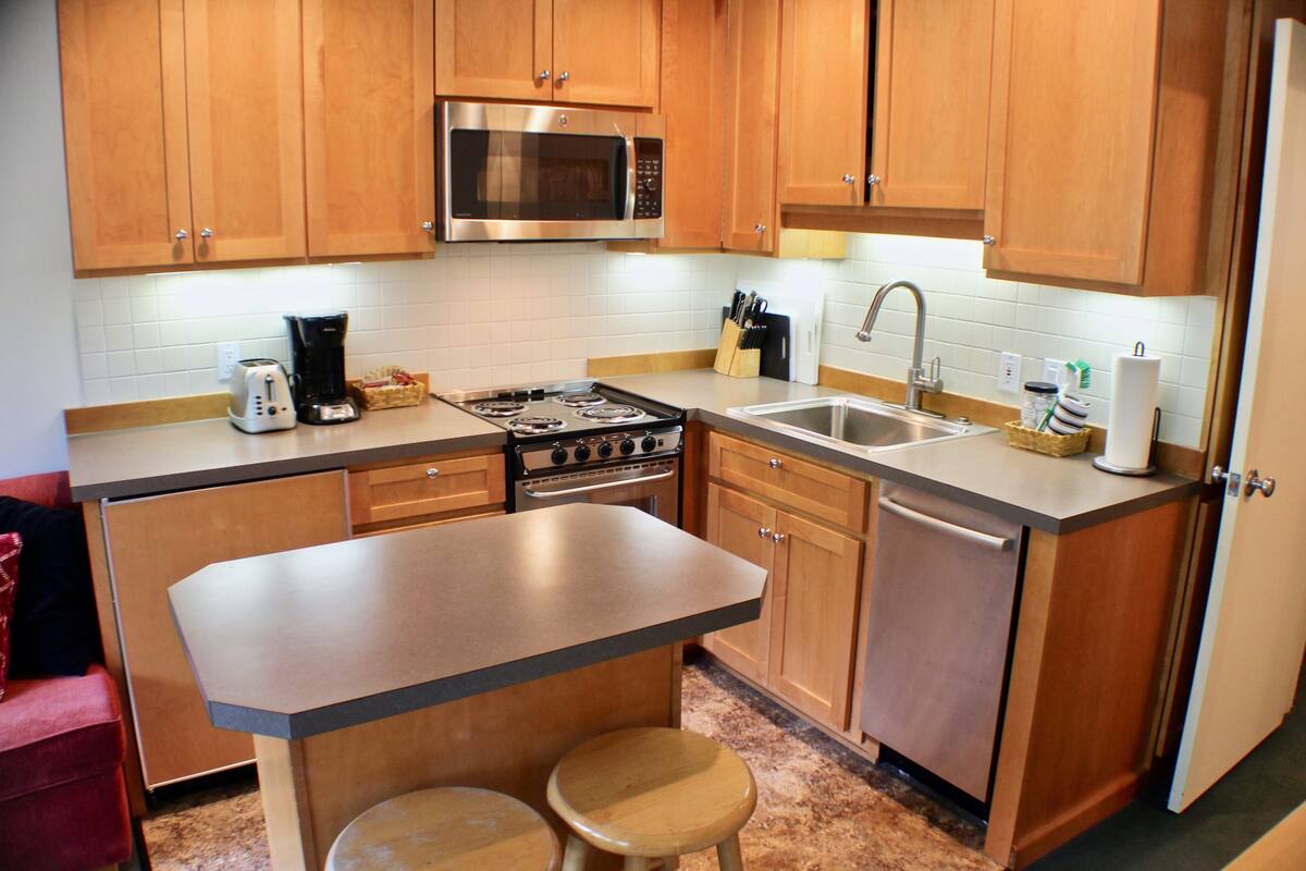A kitchen with wooden cabinets, a stainless steel microwave, a stove, and a sink.