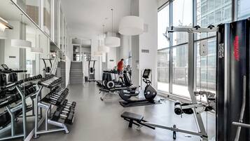 Un gimnasio moderno con diversos equipos de ejercicio, amplias ventanas y una escalera que lleva a un nivel superior.