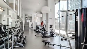 A modern gym with various exercise equipment, large windows, and a staircase leading to an upper level. - Spectacular Views Apartments (Toronto)