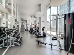 A modern gym with various exercise equipment, large windows, and a staircase leading to an upper level. - Spectacular Views Apartments (Toronto)