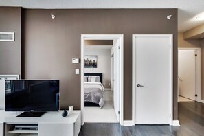 A hotel room with a bed, a TV, and a door leading to another room. - Spectacular Views Apartments (Toronto)