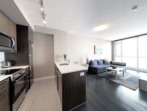 A modern kitchen with a central island, a dining area with a sofa and coffee table, and a large window providing natural light. - Spectacular Views Apartments (Toronto)