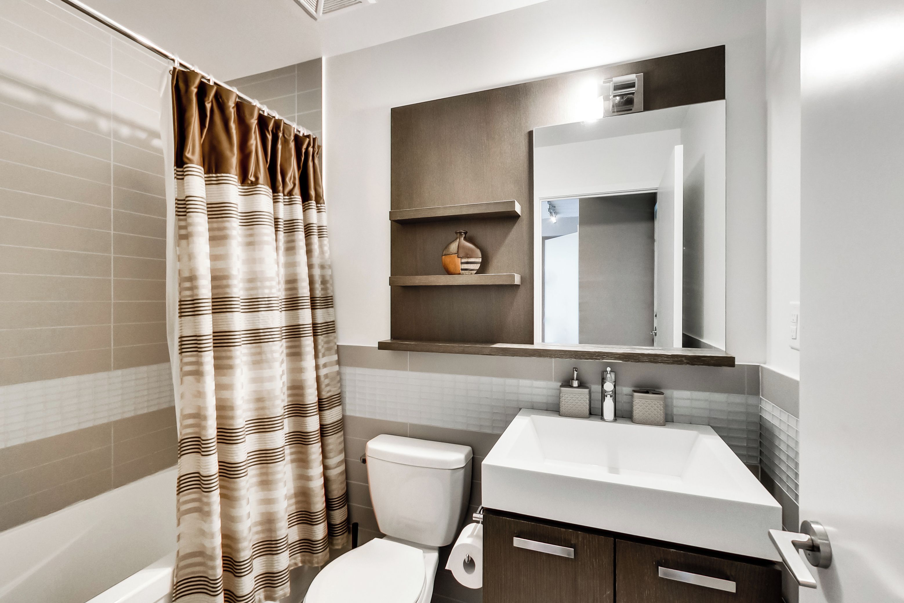 Un baño moderno con cortina de ducha, inodoro, lavabo y espejo.