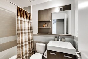 A modern bathroom with a shower curtain, toilet, sink, and mirror. - Spectacular Views Apartments (Toronto)