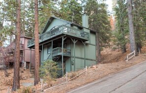 A green wooden cabin with a balcony, surrounded by trees.