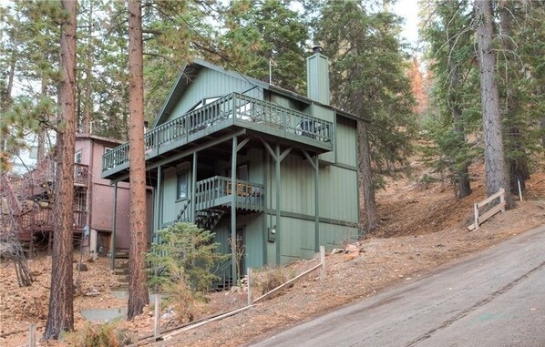A green wooden cabin with a balcony, surrounded by trees.