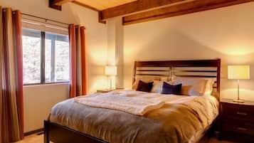 A bedroom with a large bed, wooden headboard, two bedside tables with lamps, and a window with curtains.