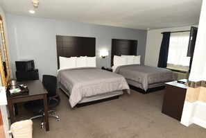 Ein Hotelzimmer mit zwei Betten, einem Schreibtisch, einem Stuhl, einem Mülleimer, einem Fernseher und einem Fenster mit Vorhängen.