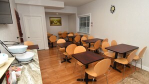 A dining area with multiple tables and chairs, a kitchen area with a microwave and a sink, and a painting on the wall. - FairBridge Hotel Atlantic City (Absecon)