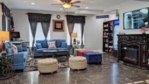 A living room with a blue sofa, ottomans, a coffee table, a fireplace, and a television displaying a labor day sale. - FairBridge Hotel Atlantic City (Absecon)