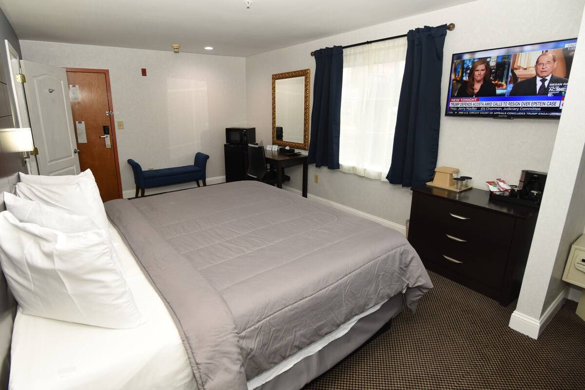 A hotel room with a bed, a desk, a chair, a TV, and a mirror.