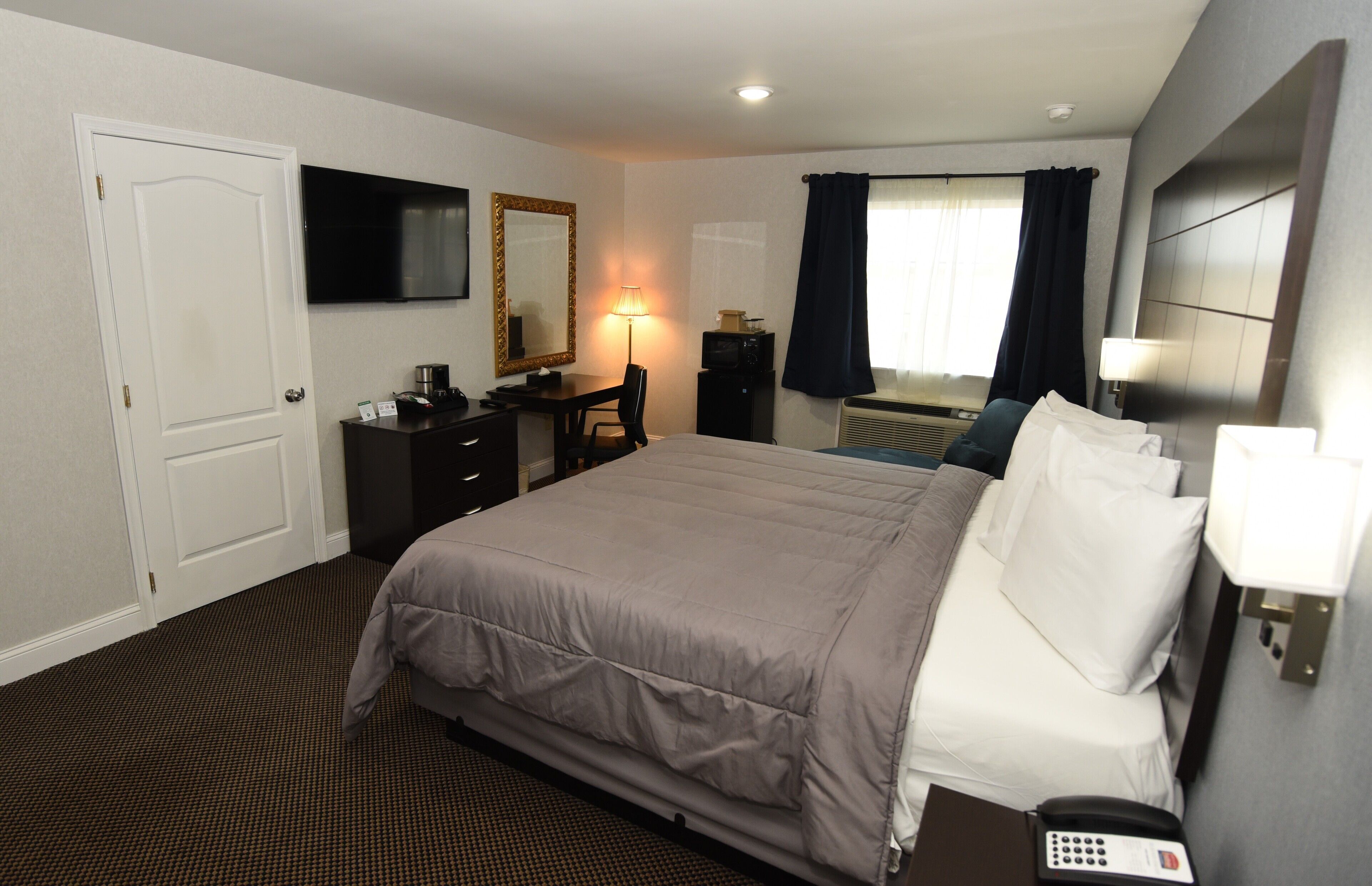Habitación de hotel con una cama grande, un escritorio con silla, televisión, espejo, lámpara de escritorio y teléfono.