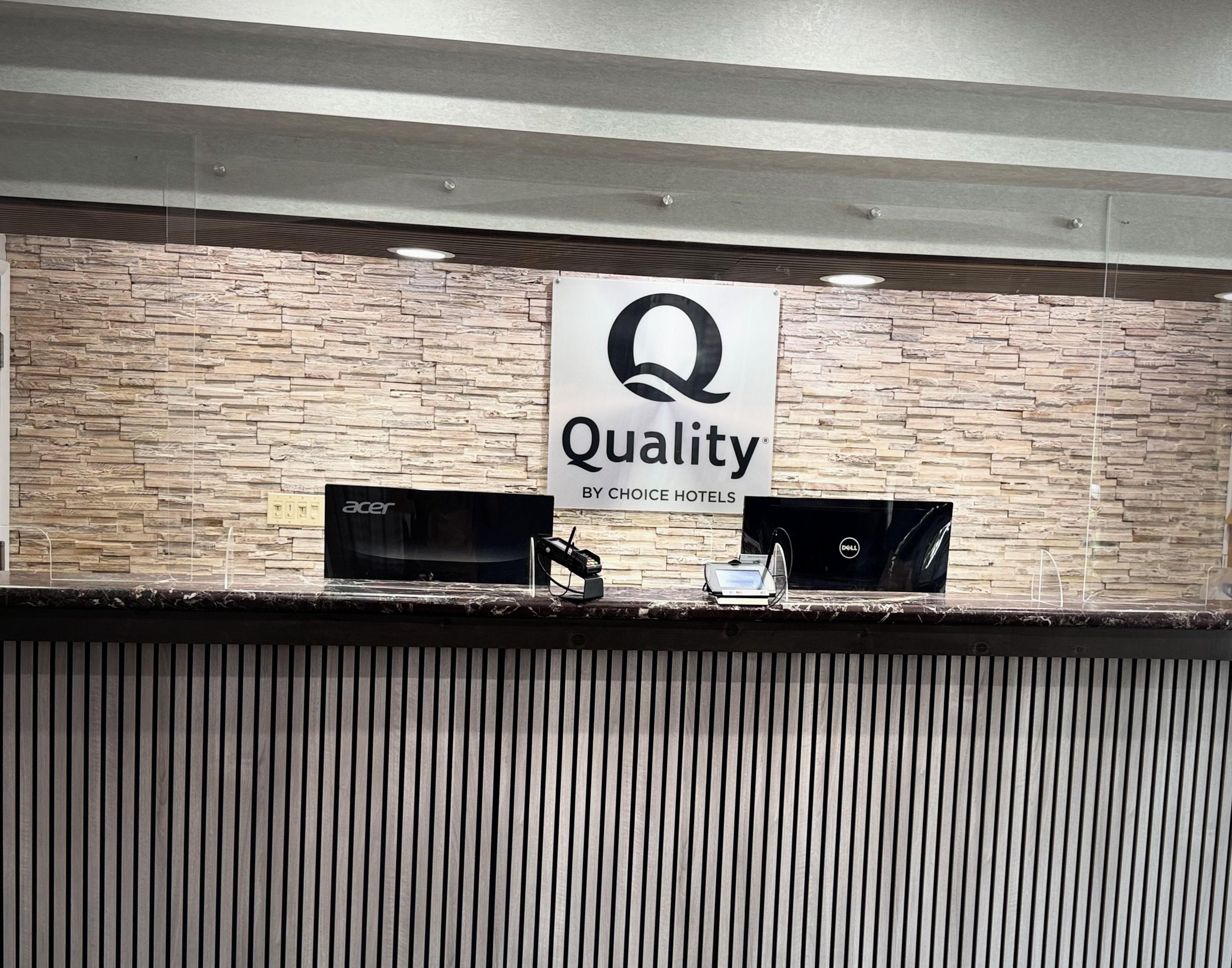 Una mesa de recepción con un letrero que dice 'Quality by Choice Hotels' y dos portátiles encima.