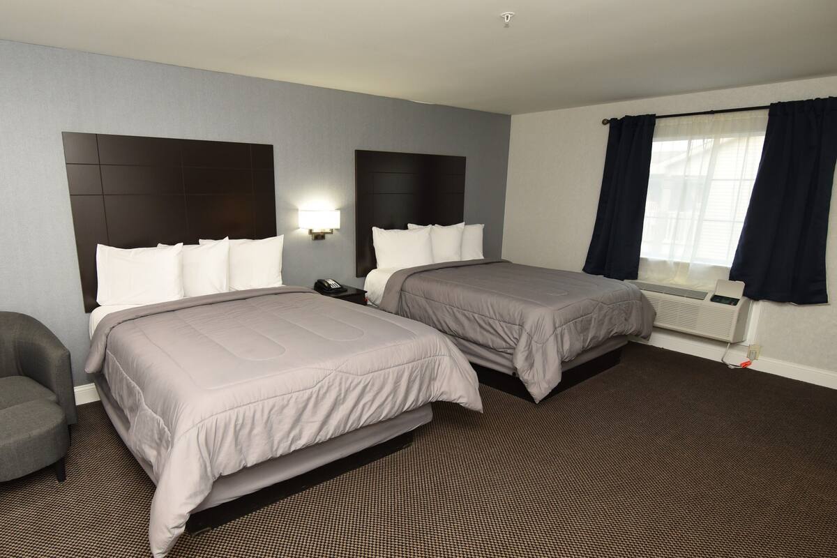 A hotel room with two beds, a chair, a nightstand with a phone, and a window with curtains.