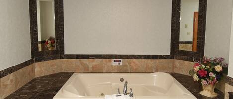 Una bañera grande y rectangular con un grifo central y dos grifos laterales, rodeada de baldosas de mármol.