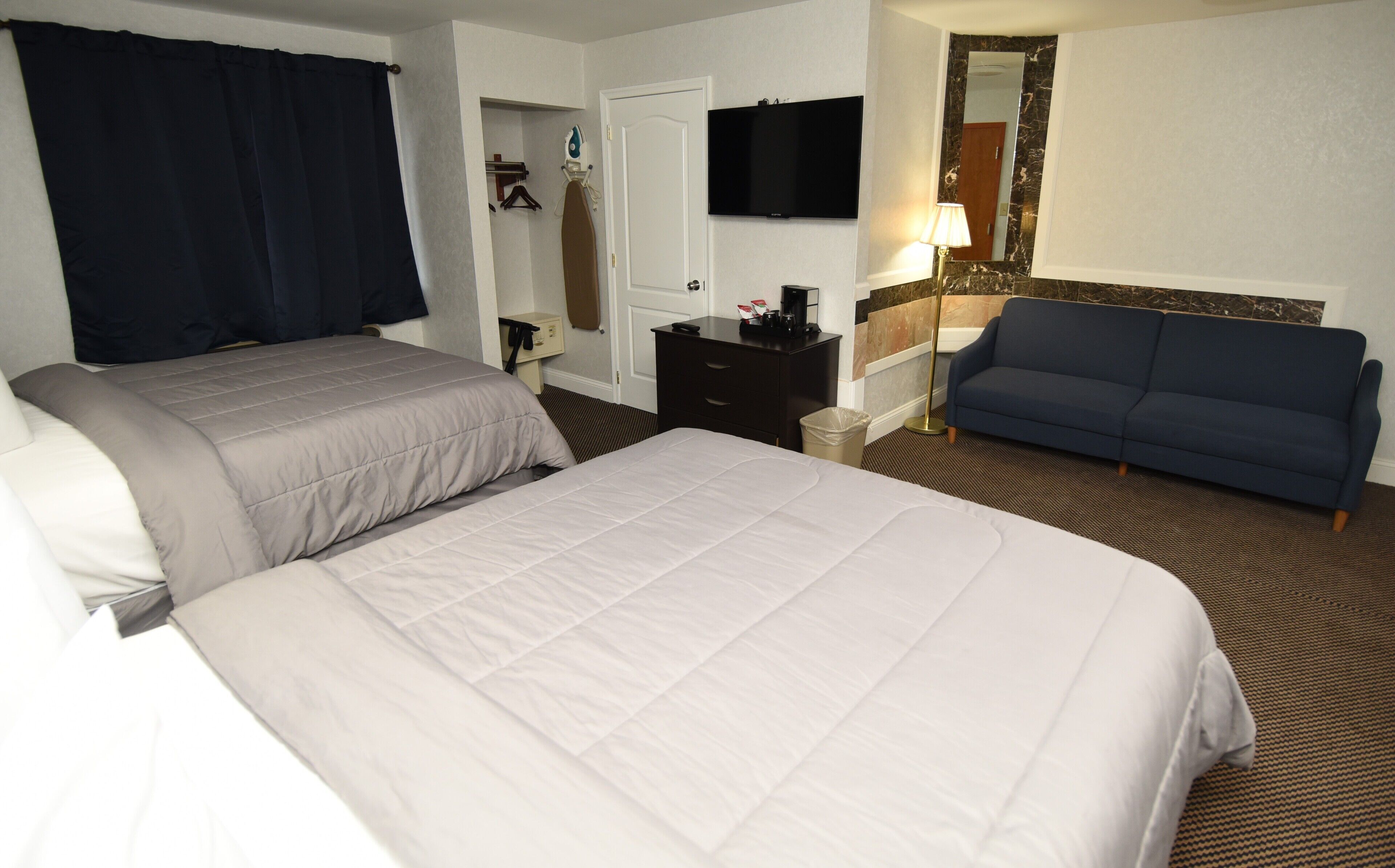 A hotel room with two beds, a TV, a desk, a chair, and a sofa.