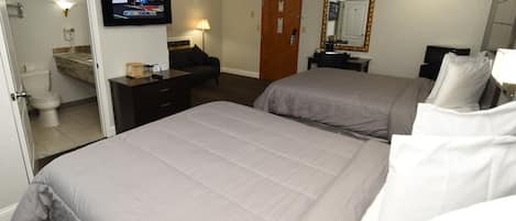 A hotel room with two beds, a TV, a desk, a mirror, and a bathroom.