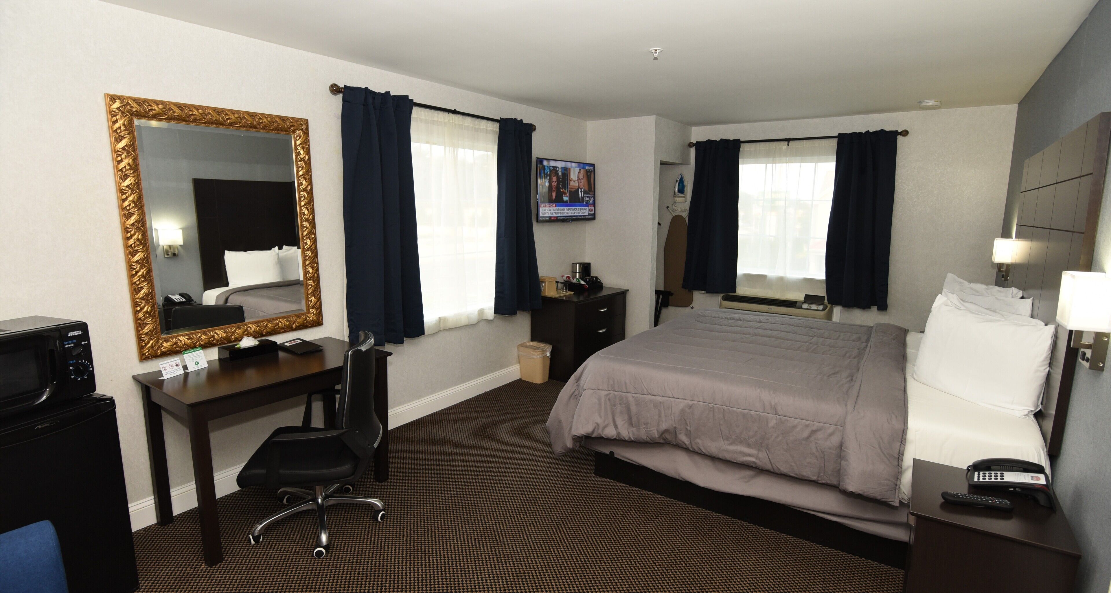 Una habitación de hotel con una cama, un escritorio con silla, un televisor, un microondas y un espejo grande.