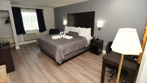 A hotel room with a bed, bedside tables, a desk, a chair, a lamp, a telephone, and a window with curtains. - FairBridge Hotel Atlantic City (Absecon)