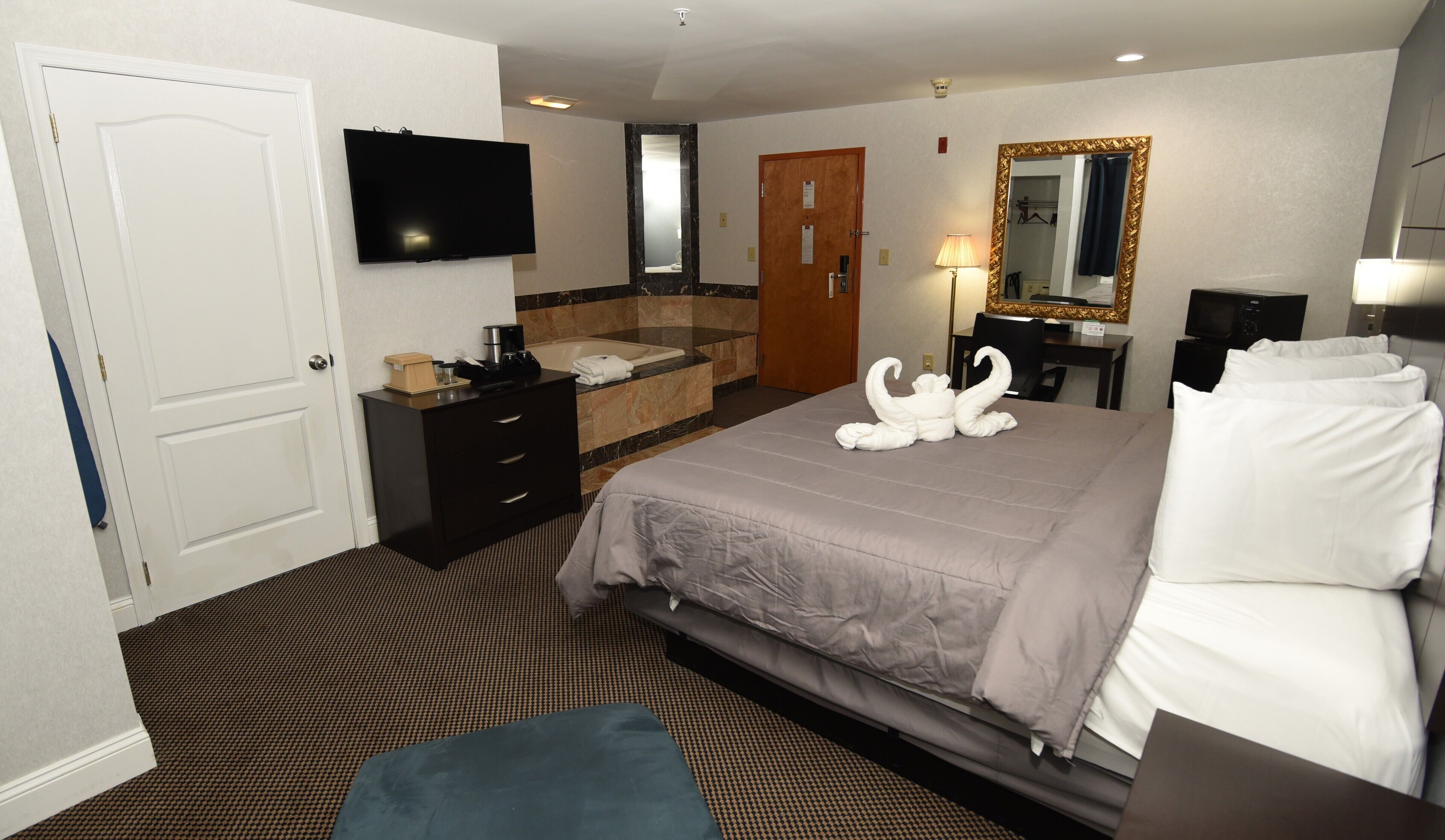 A hotel room with a bed, a TV, a bathroom with a sink and mirror, and a desk with a lamp.