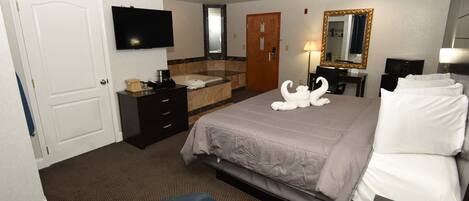 A hotel room with a bed, a TV, a bathroom with a sink and mirror, and a desk with a lamp.
