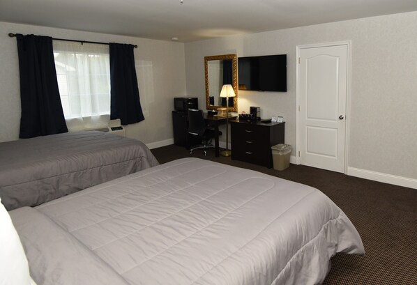 A hotel room with two beds, a desk with a computer, a chair, a TV, and a door.