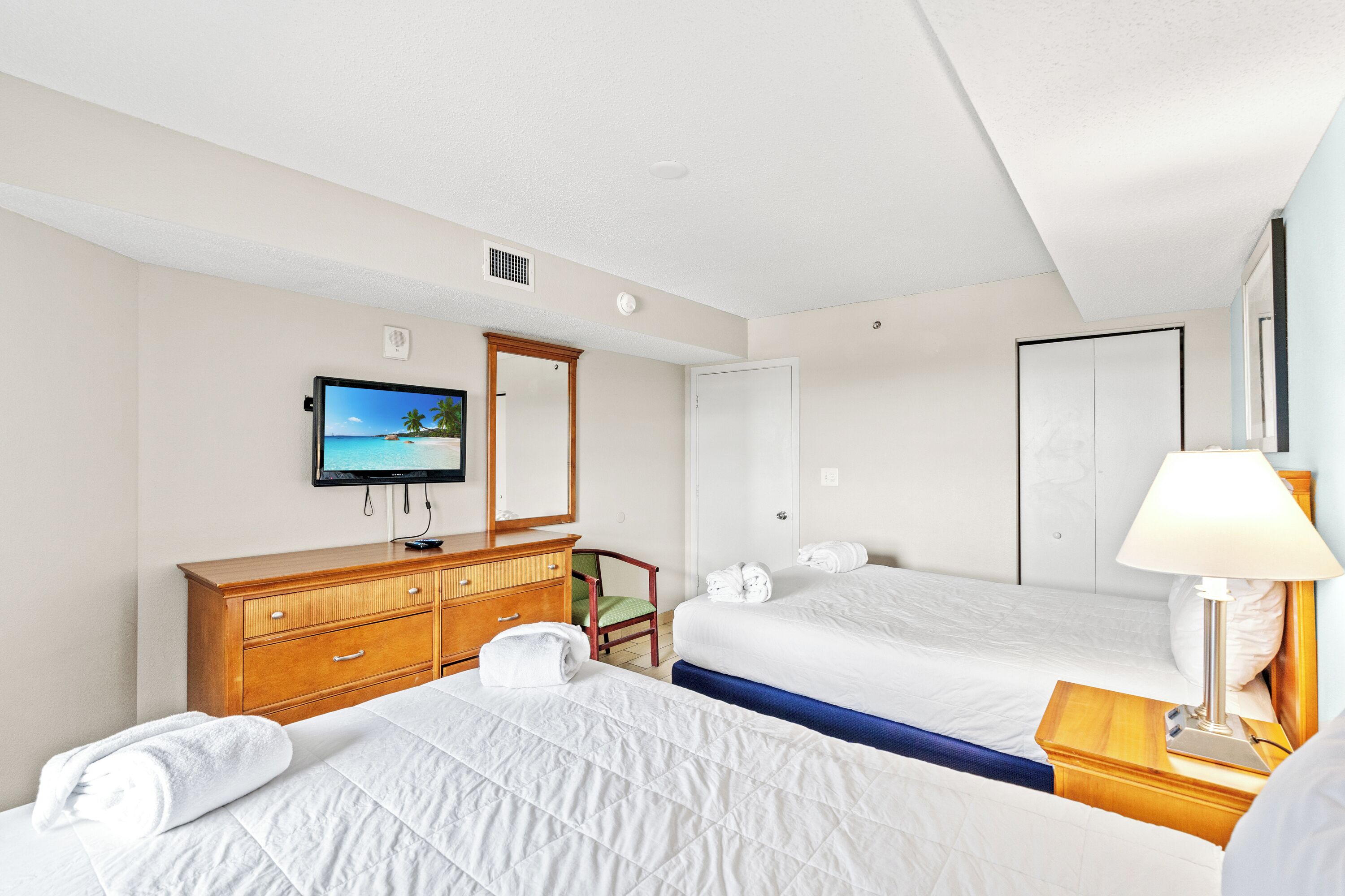 A hotel room with two beds, a wooden dresser, a television, and a mirror.