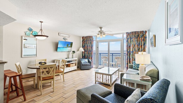 A spacious living area with a dining table, chairs, a sofa, and a balcony with curtains.
