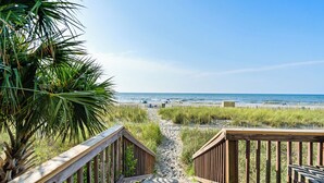 A wooden boardwalk leading to a beach with a clear view of the ocean.