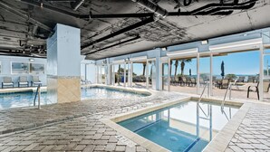 An indoor swimming pool with a tiled floor, surrounded by lounge chairs and a view of the ocean.