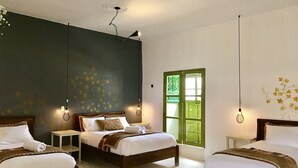 Habitación de hotel con tres camas, una pared oscura con motivos florales y una puerta verde.