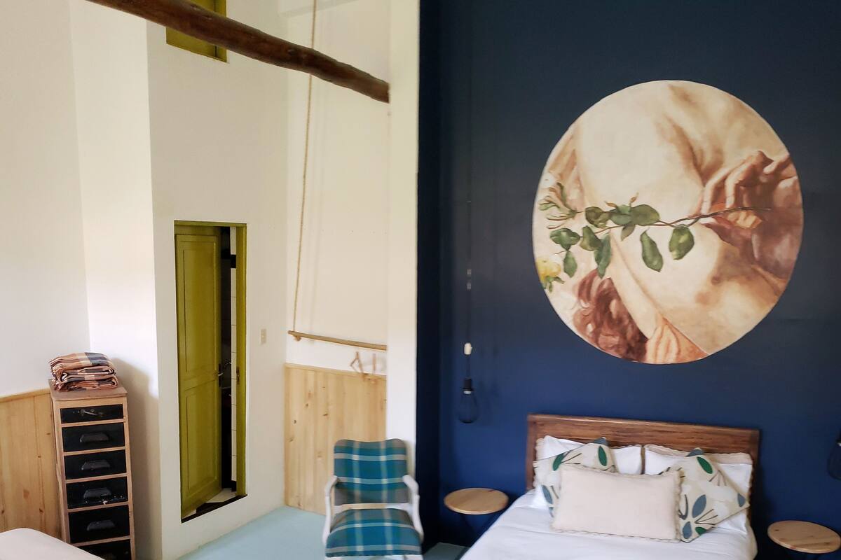 Ein Schlafzimmer mit einem Bett, einem Sessel, einem kleinen Tisch und einem Wandbild.