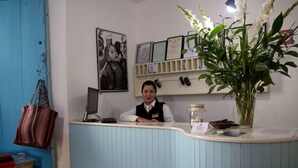 Un mostrador de recepción con una computadora, diplomas enmarcados, un florero con flores y una pared azul.