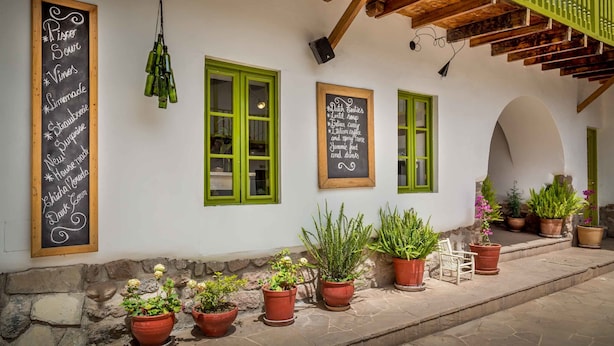 Un edificio con contraventanas verdes, plantas en macetas y un menú en pizarra que enumera platos como 'Piper Sour Vines' y 'Dutch Classics'.