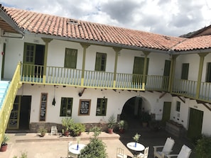 A traditional building with a tiled roof, a balcony with yellow railings, and a courtyard with potted plants and outdoor seating. - Niños Hotel Fierro (Cusco)