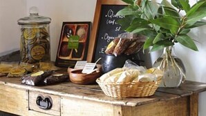 Una mesa de madera rústica con frascos de conservas, un cuadro enmarcado, un menú en una pizarra y una planta en maceta.