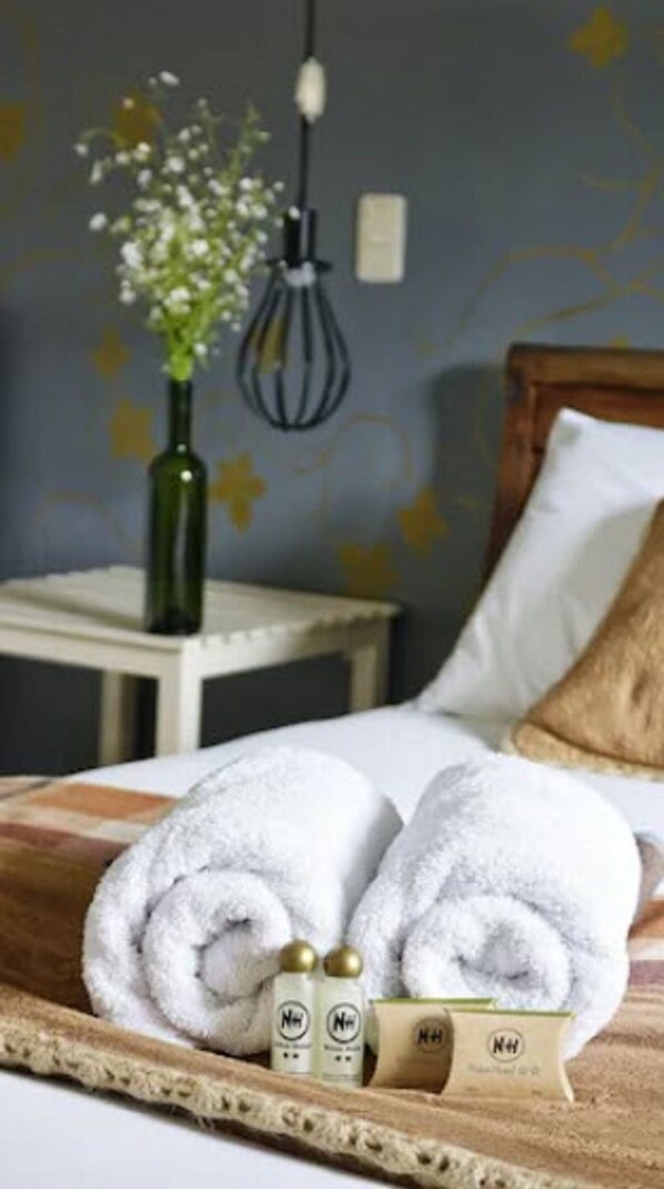 A neatly made bed with two white towels, a small wooden tray with toiletries, and a vase with flowers on a nightstand. - Niños Hotel Fierro (Cusco)