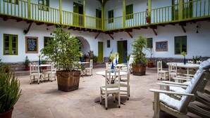 Un patio con suelo de piedra, sillas blancas y plantas en macetas.