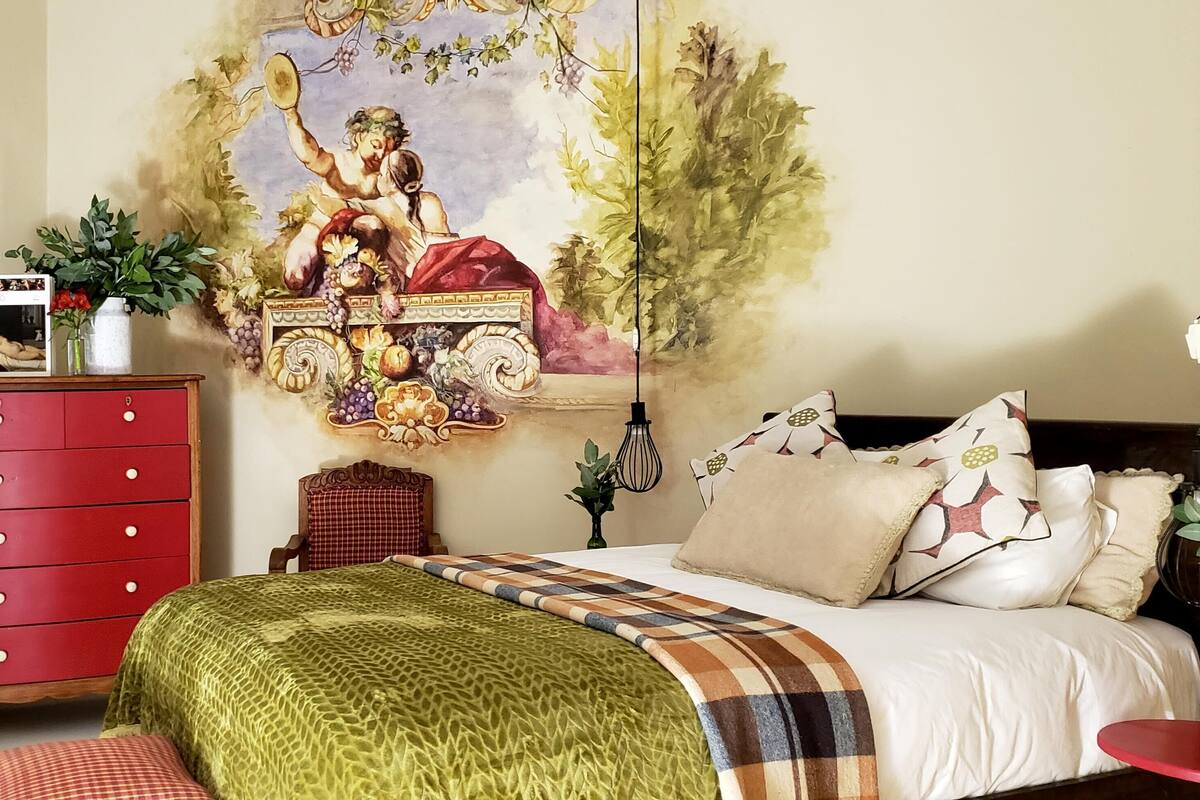 Ein Schlafzimmer mit einem Bett, einer roten Kommode, einem Wandbild und einem kleinen Tisch mit einer Pflanze.