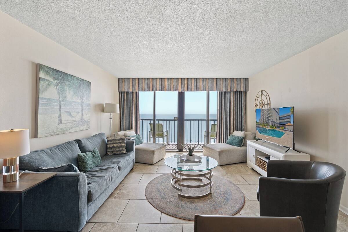 A modern living room with a sofa, armchair, glass coffee table, and a TV on a stand.
