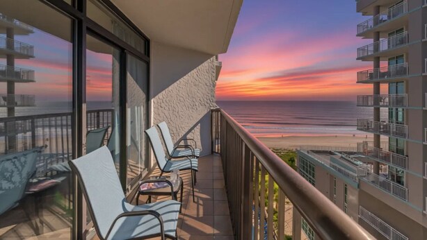 A balcony with chairs overlooking a beach at sunset. - Beach Colony Resort by Elliott Beach Rentals (Myrtle Beach)