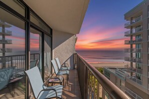 Un balcon avec des chaises donnant sur une plage au coucher du soleil.