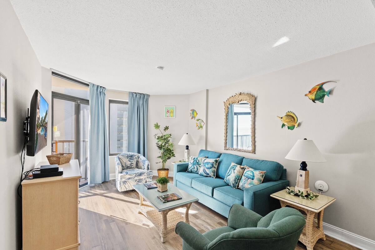A living room with a blue sofa, a green armchair, a coffee table, and a TV on a stand.