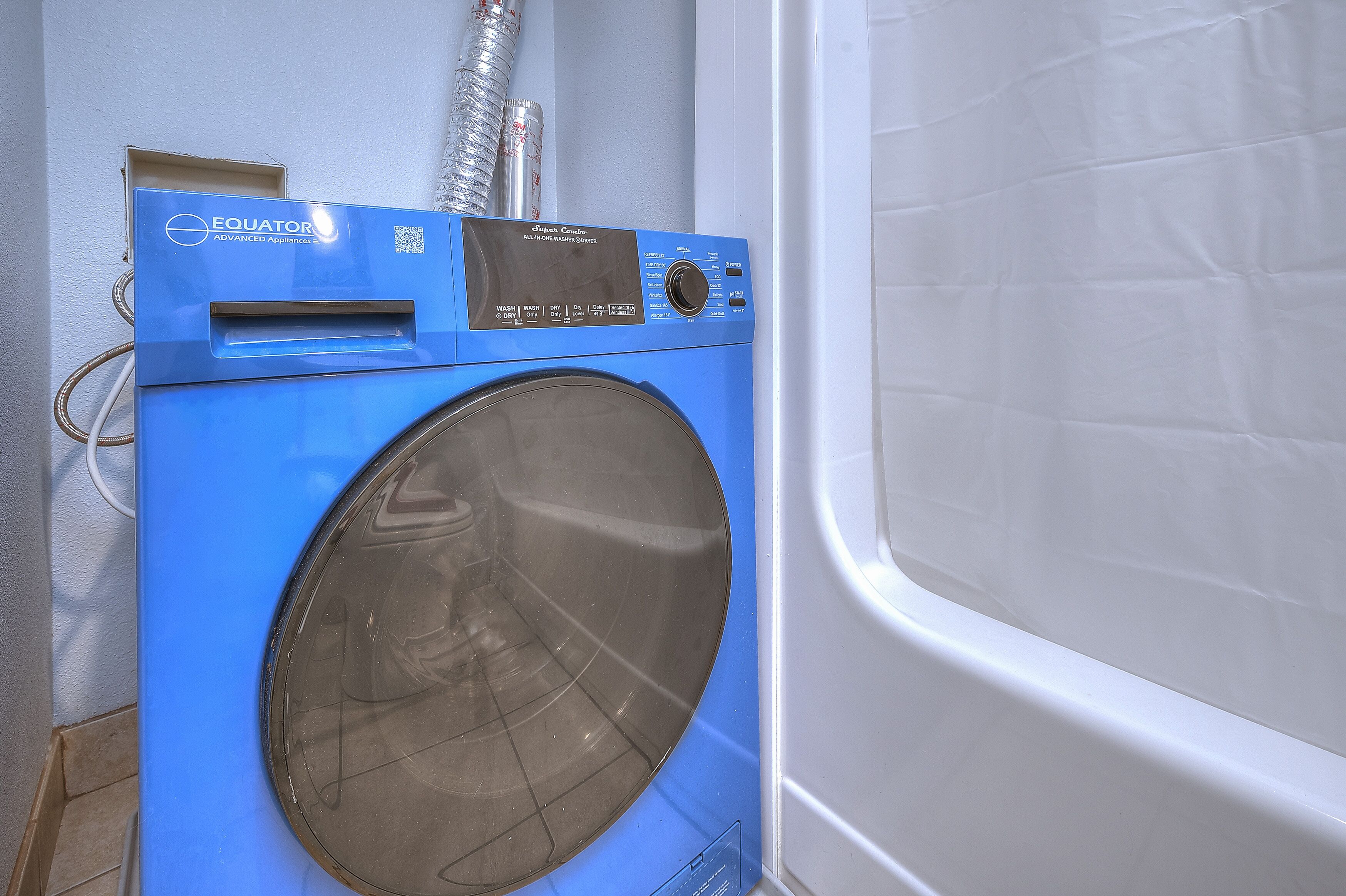 A blue washing machine with a control panel and a transparent door, situated next to a white bathtub.