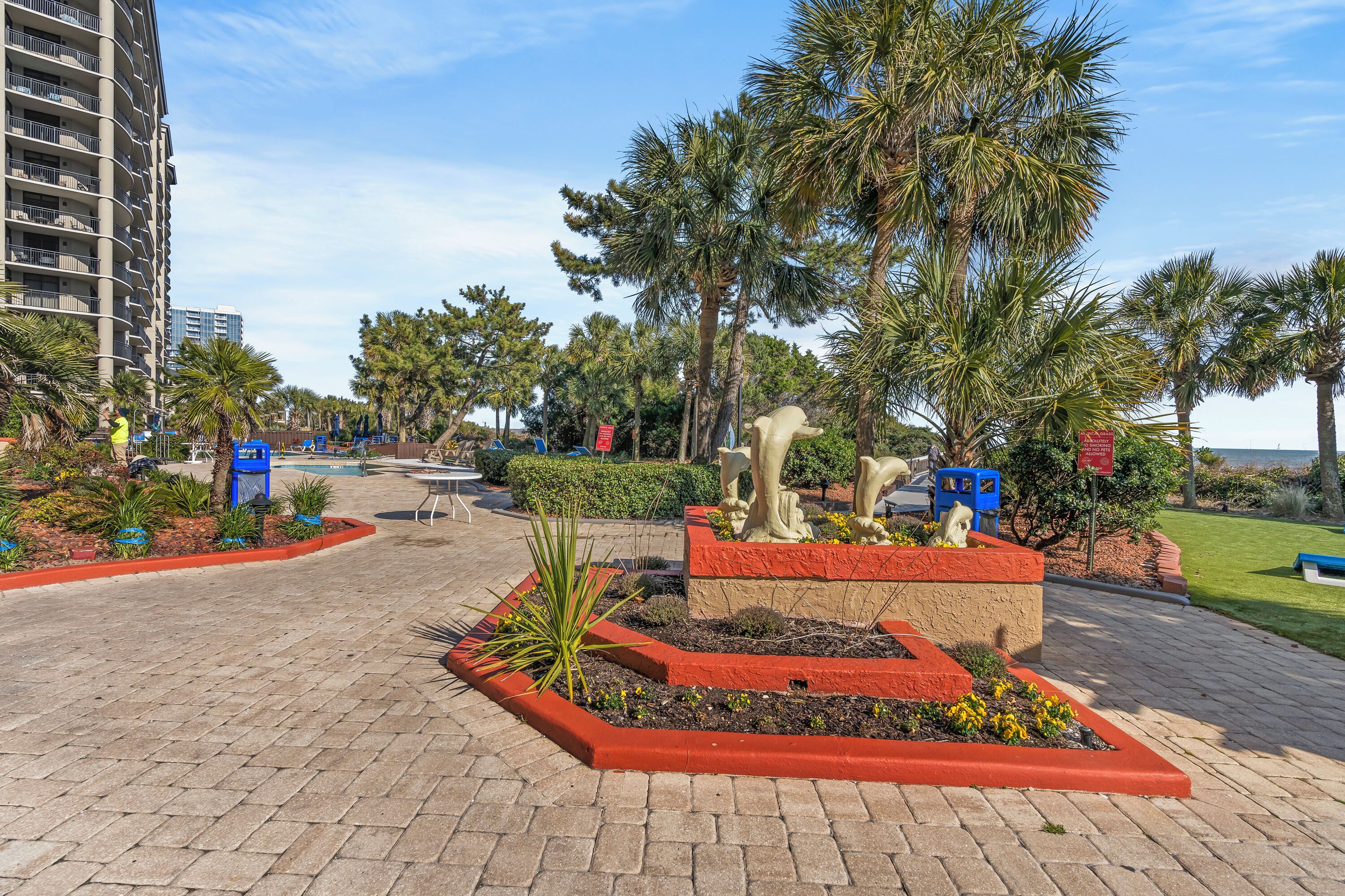 Un espace aménagé avec un parterre central, des palmiers et un chemin pavé.