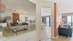 A modern kitchen with granite countertops, a sink, and a dining area with a sofa and a table. - Beach Colony Resort by Elliott Beach Rentals (Myrtle Beach)
