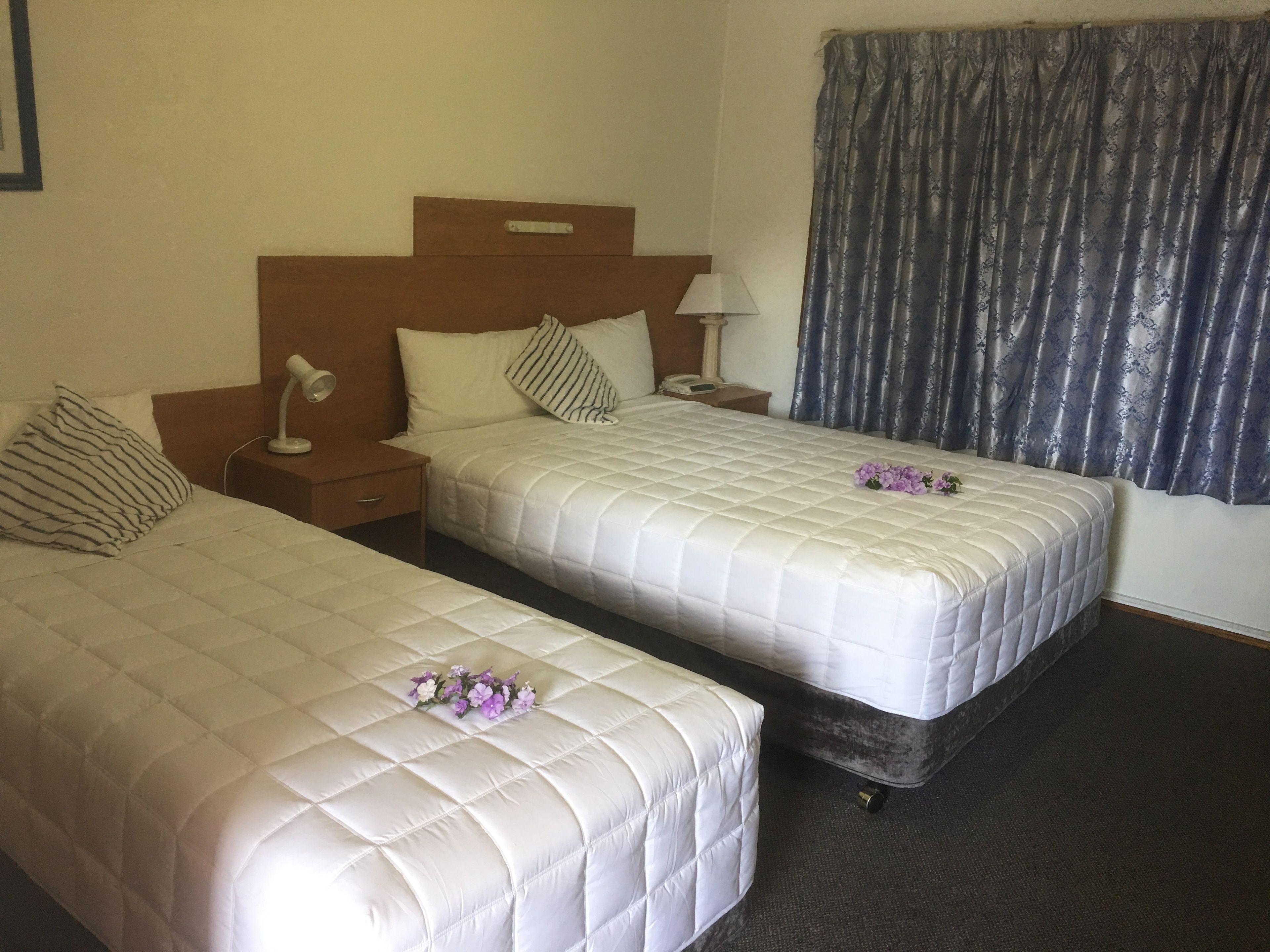 Ein Hotelzimmer mit zwei Betten, einem Nachttisch mit Lampe, einem Telefon und einem Fenster mit Vorhängen.