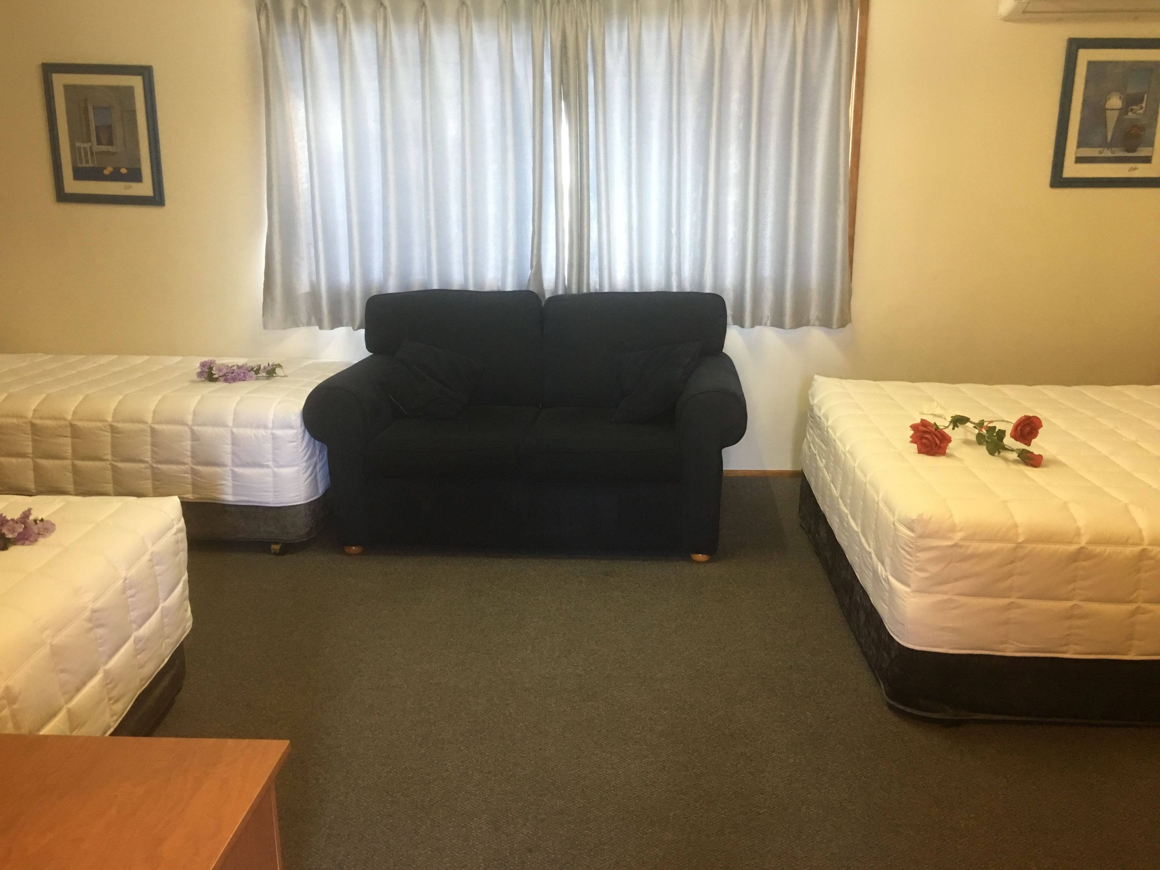 A room with two single beds, a sofa, a wooden table, and a window with curtains.